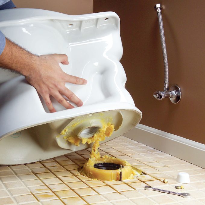 man lifting a Toilet to reveal the Wax Ring on the floor