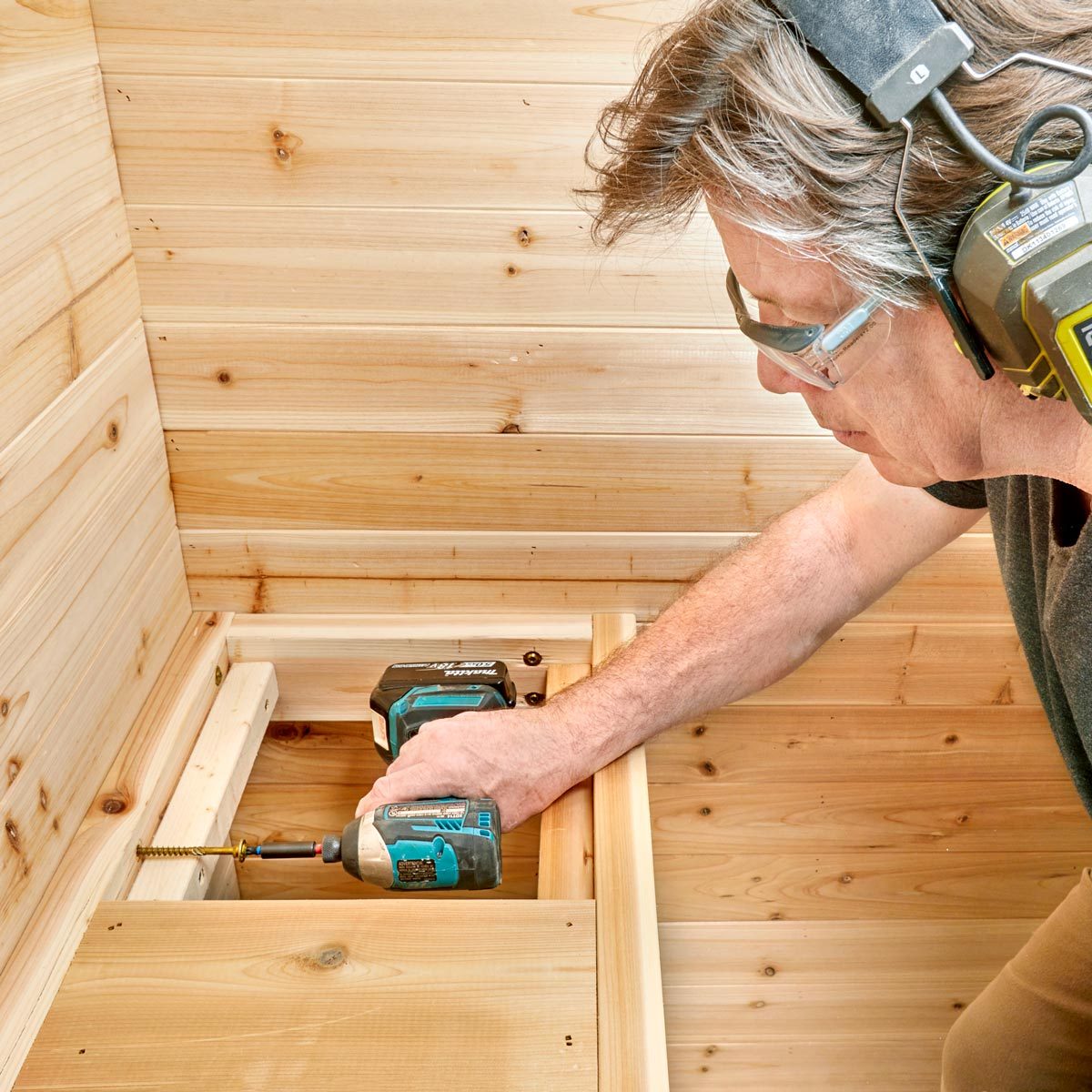 man using a drill to install the sauna bench inside the sauna