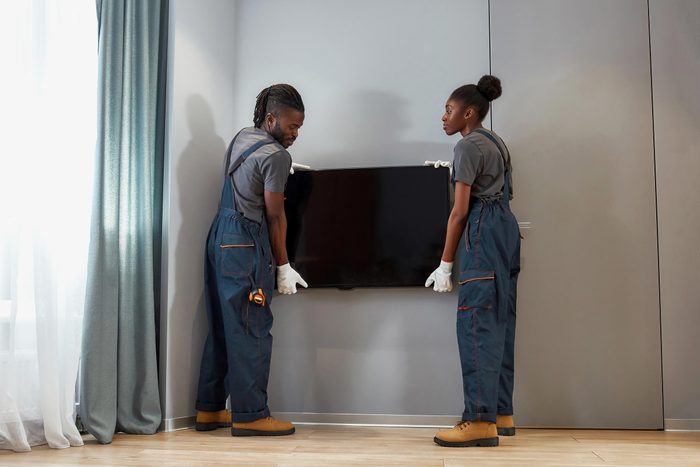 Two handy persons hanging flat screen television on wall