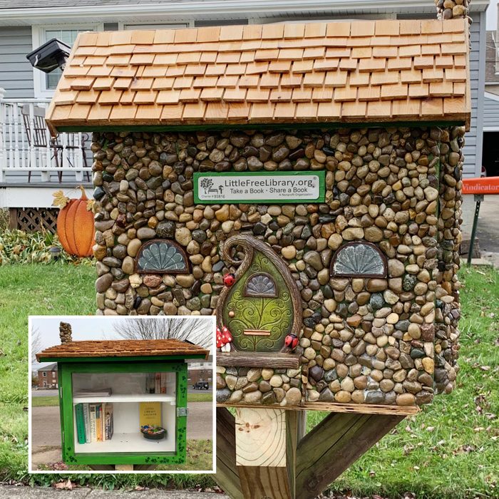 a little free library intricately decorated with stones, miniature doors and windows to look like a fairy house