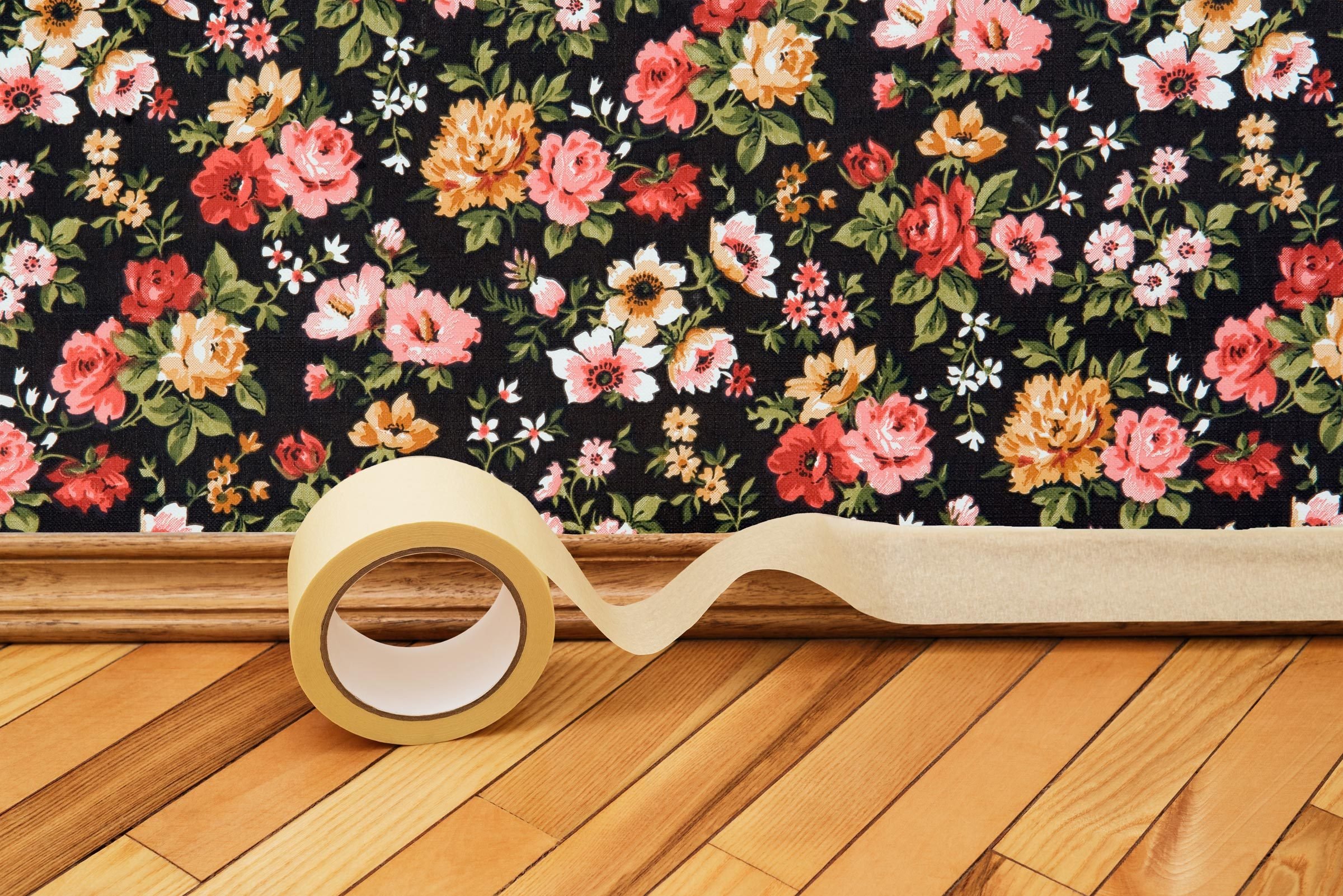 putting masking tape on the Baseboard with a floral wallpaper wall