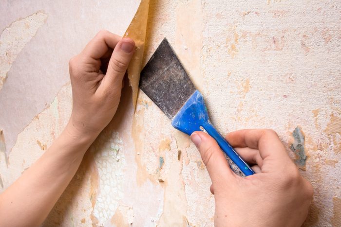 Hands removing wallpaper from wall with spatula