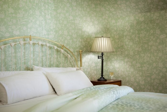 Pale Green Bedroom with small repeating flower wallpaper, bed with a lamp on a side table next to it