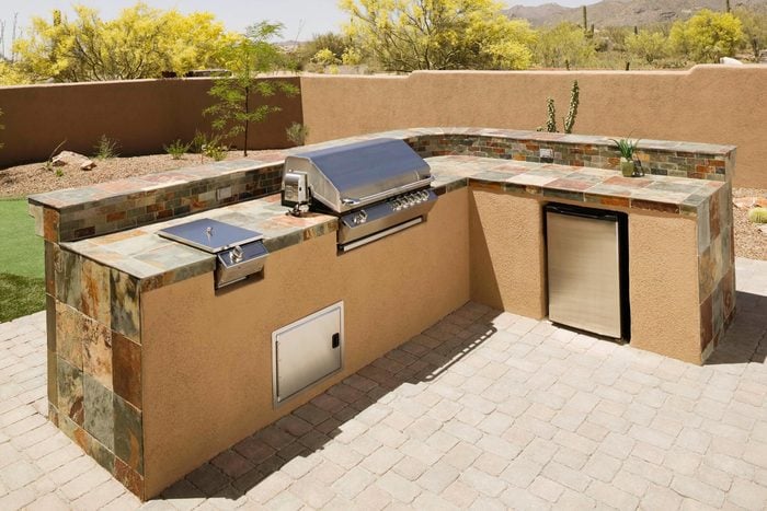 outdoor kitchen with a grill and stone tile counter tops in a desert backyard