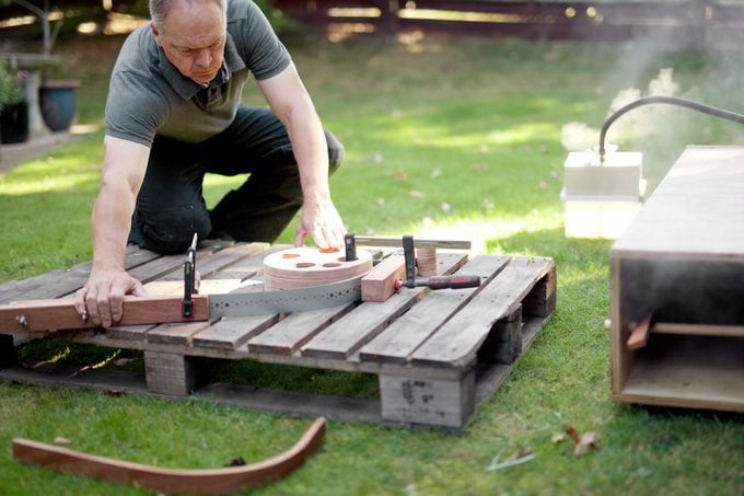 a man woodworker steam bending wood on a pallet outside in the grass