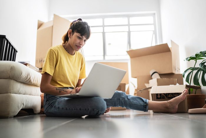 Young woman using laptop on the floor in search of a new apartment with moving boxes in the background