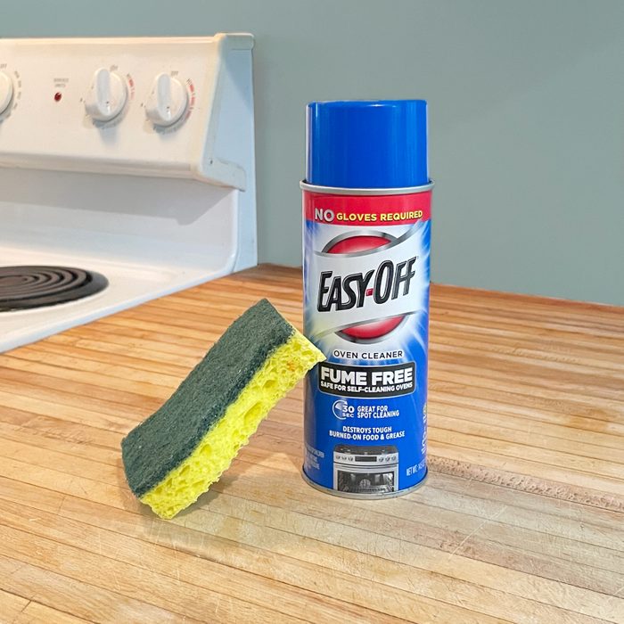 a can of oven cleaner sitting on a wooden kitchen counter top with a sponge and an oven in the background