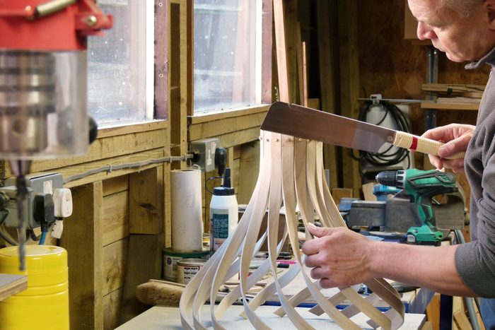 A carpenter in his workshop, is making a wooden pendant lampshade using oak, which has been bent and twisted into shape using traditional wood steam bending techniques
