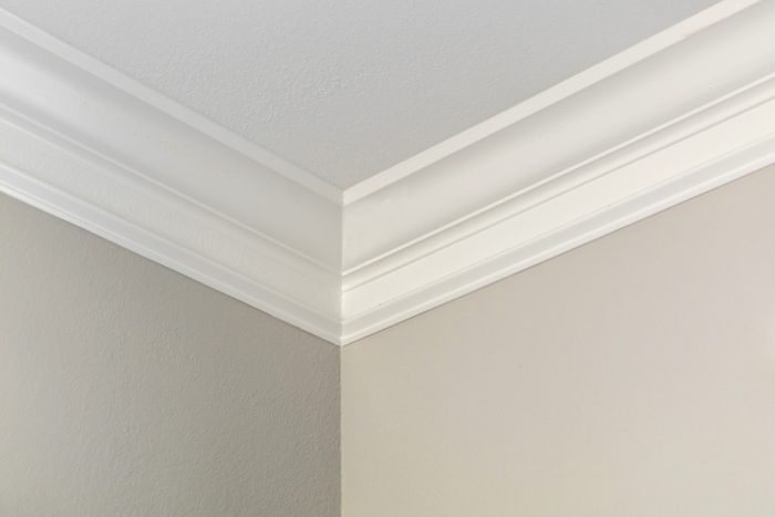 The corner of a house near where the beige neutral walls and white ceiling meet with large 6 inch detailed crown moulding in a new construction home
