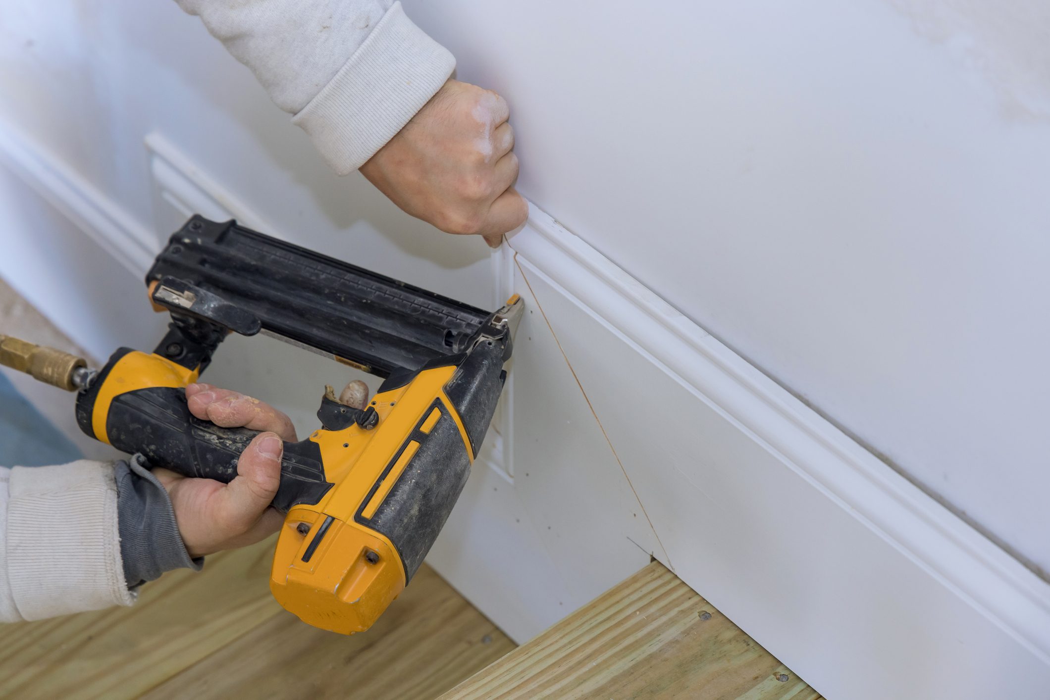 The carpenter uses a brad nail gun for the purpose of nailing the base molding trim