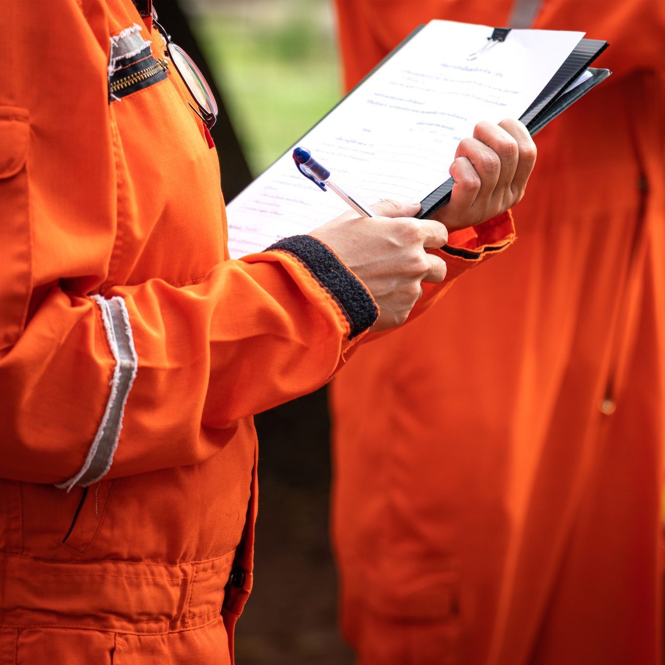 A safety supervisor in an orange jumpsuit is writing down on paper for taking note during safety audit at the operation work site