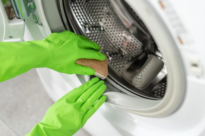gloved hands clean moldy washing machine with open door