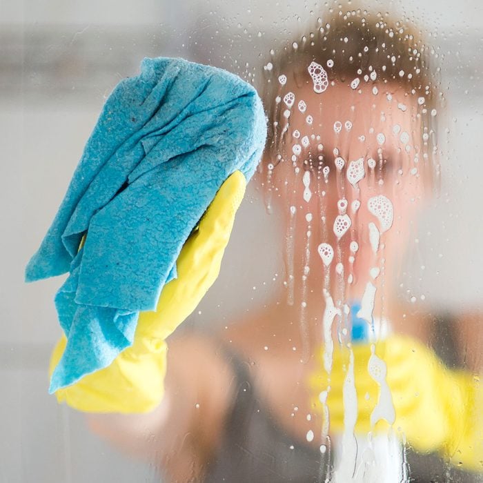 person cleaning glass shower pane with cloth and spray bottle