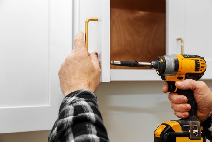 close up of a man with a drill installing gold cabinet handles on white kitchen cabinet doors