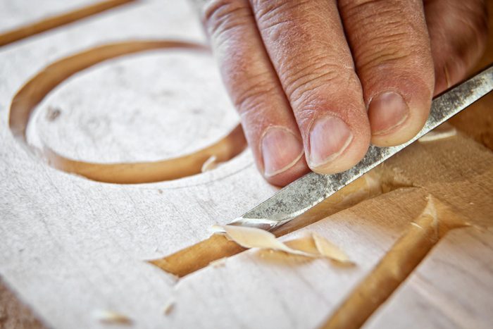 Macro photo of a skilled carpenter using a chisel to engrave letters in a wooden sign
