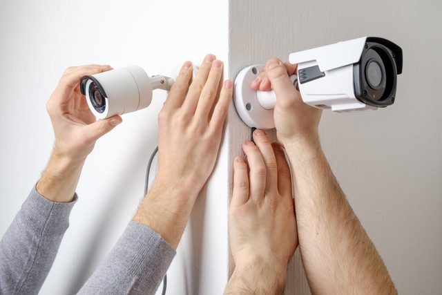 two sets of hands installing security cameras on the corner of a room where the two walls meet