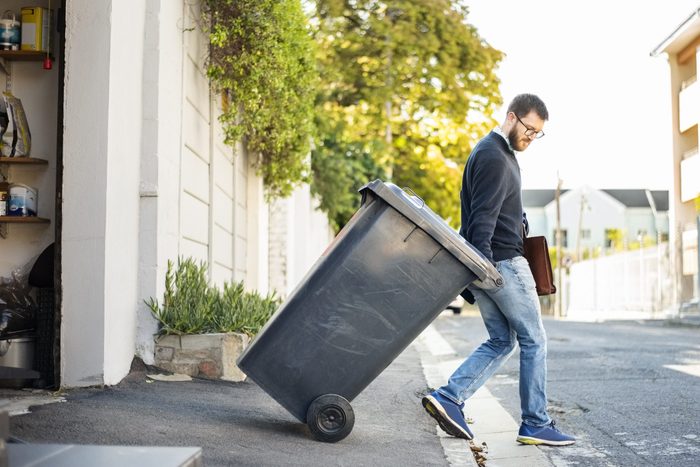 Man pulling a wheeled dumpster out of his garage while going to work