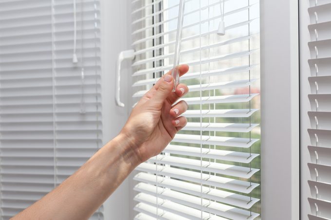 close up of hands closing the blinds on a window
