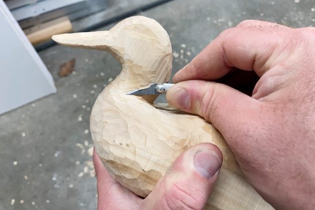 hand carving a wooden duck with a small exacto knife