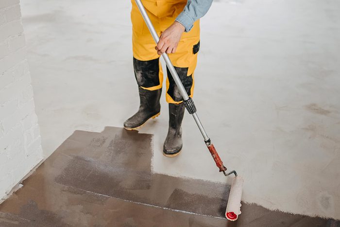 man in yellow work overalls putting epoxy on a concrete floor in a basement