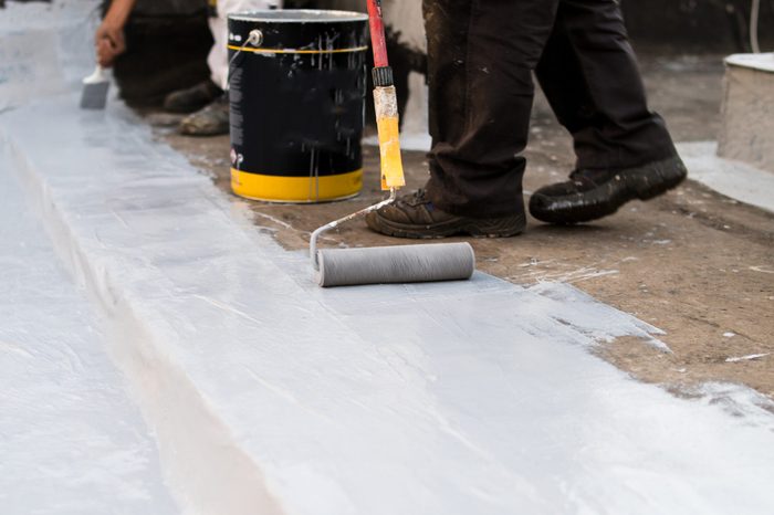 Applying waterproofing epoxy with a paint roller to a concrete floor
