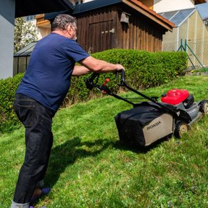 A man mowing the lawn in his yard with a Honda HRX76 lawn mower.