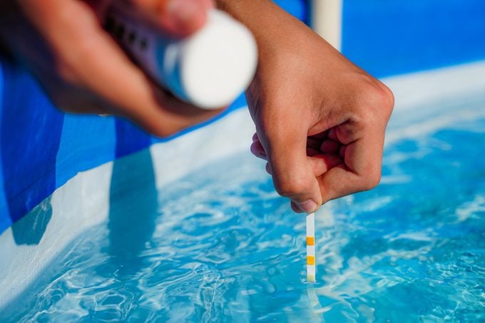 hands dipping a PH test strip into a swimming pool