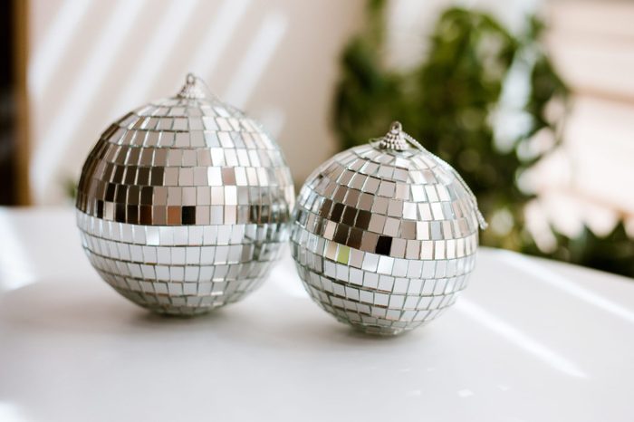 Two disco balls on white table in sunny room with plants on background.