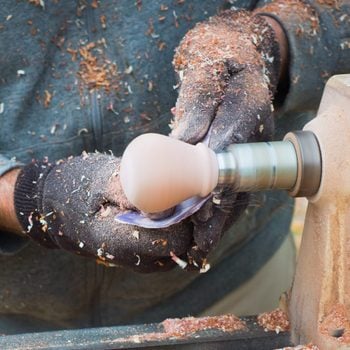 close up of a man wearing gloves woodturning and working a knob on a lathe