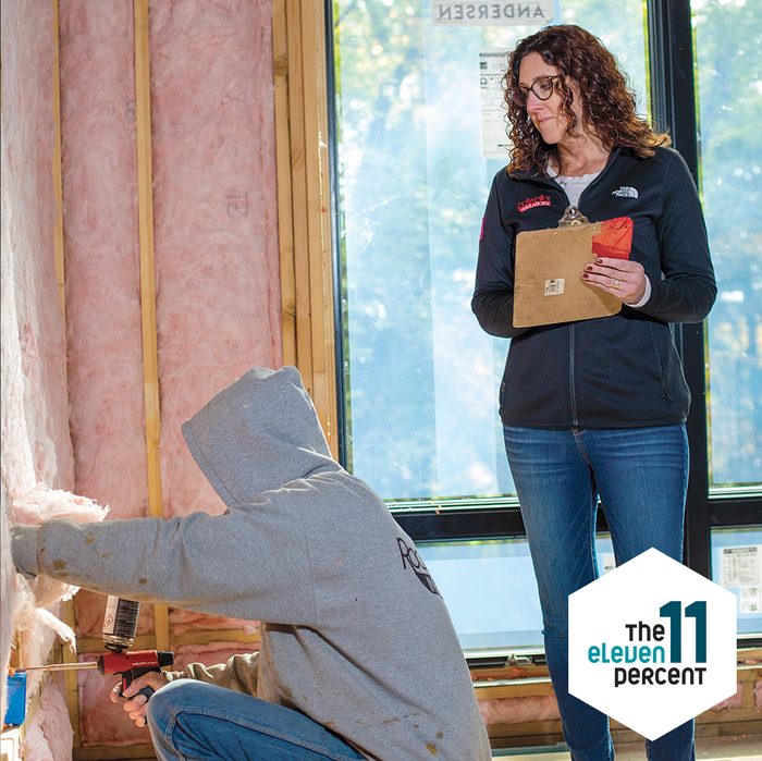 Renee Wilson with a clipboard in a house that is being insulated by a young man in a grey hoodie