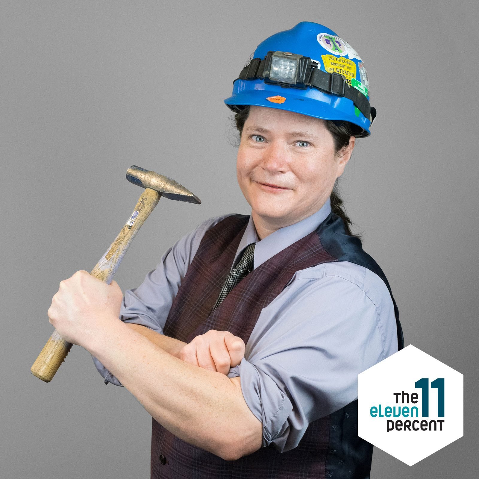 portrait of Soph Davenberry wearing a hard hat and holding a hammer showing their muscles
