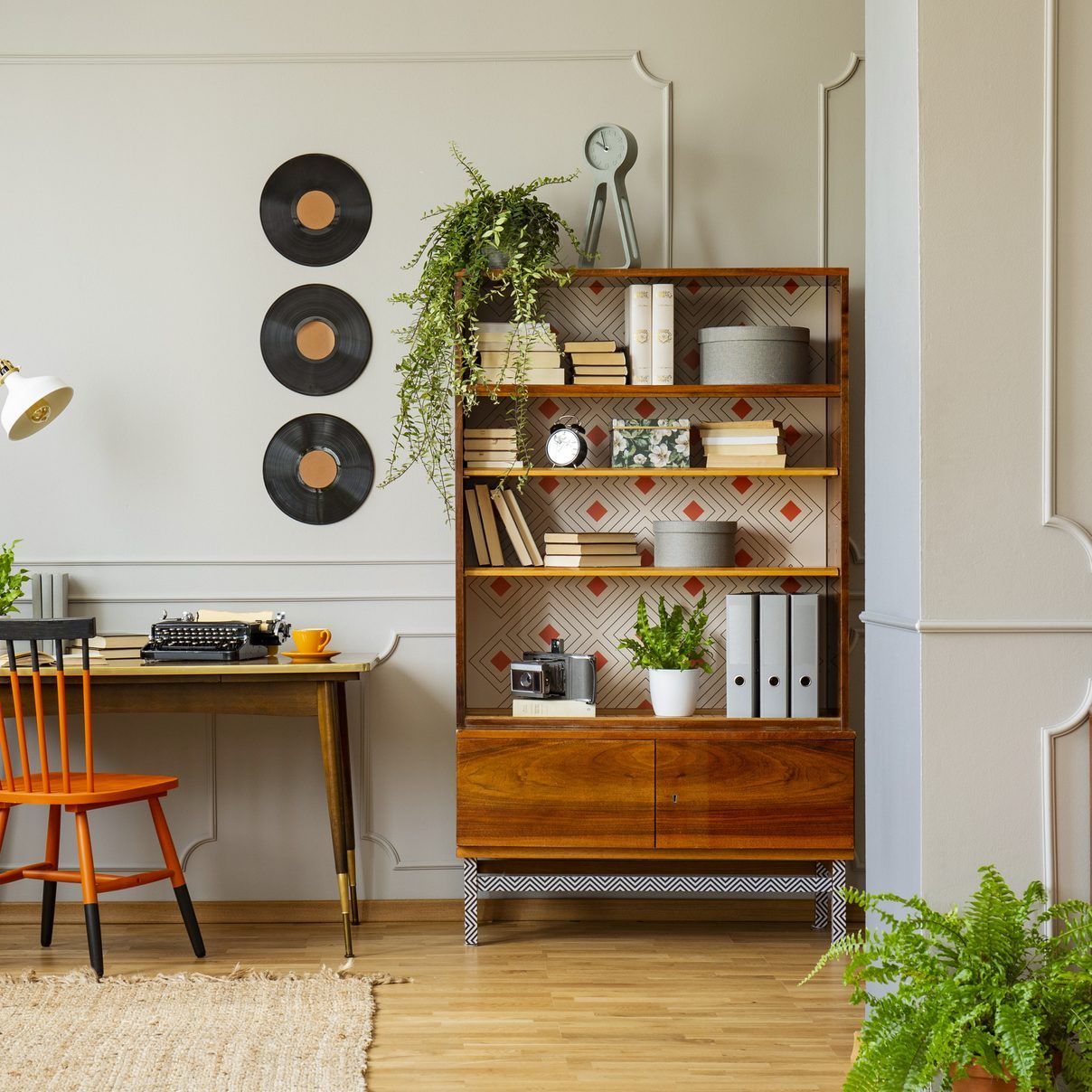 Виниловые пластинки украшают серую стену с лепниной и деревянной мебелью в ретро-интерьере домашнего офиса для писателя.  Настоящее фото.