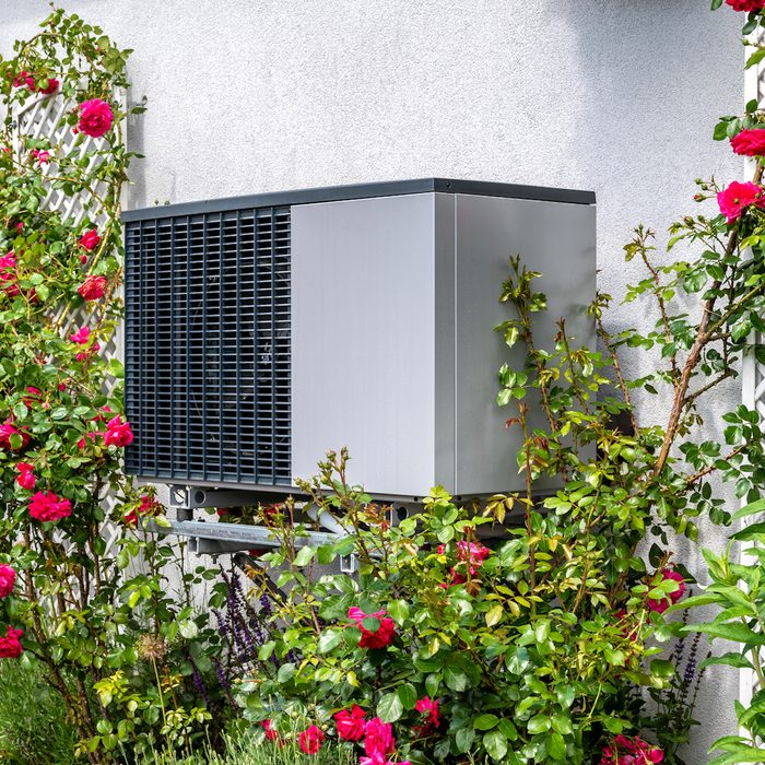 Outdoor Unit Of Heat Pump Heating Of Residential House Framed By Roses