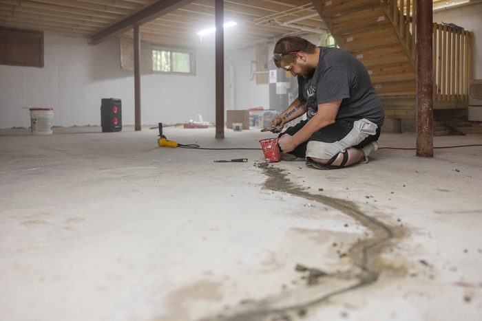 Basement waterproofing. Worker sealing cracks in basement floor to prevent flooding and mold.
