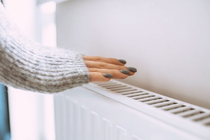 Cold Radiators In Apartment. Female Hands In Sweater Trying To Get Warm From Radiator Near Wall