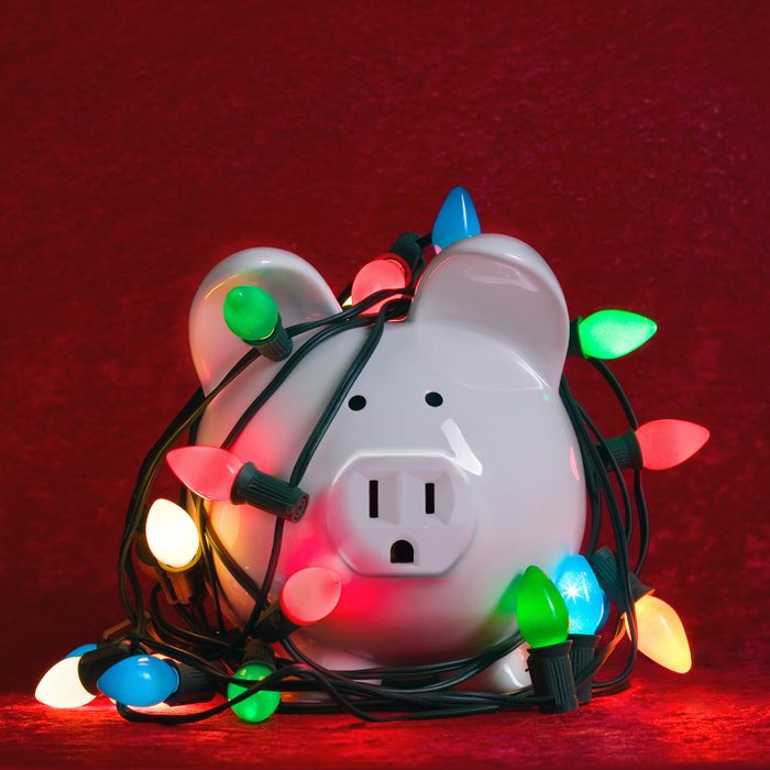 White piggy bank with an electric outlet nose wrapped in old christmas lights on an all red background
