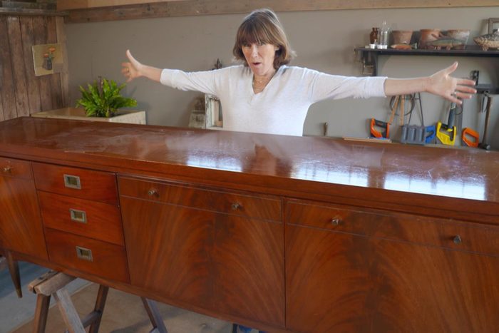 a woman with her arms outstretched standing behind a newly restored wooden dresser