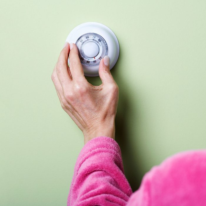 woman hand adjusting an old manual thermostat on a green wall