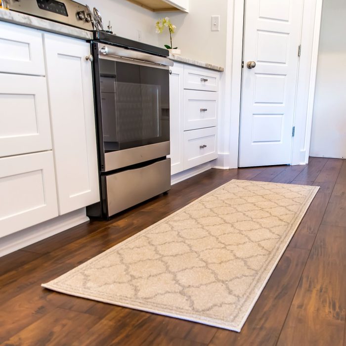 close up of a throw rug in a kitchen with white cabinets and a wood floor
