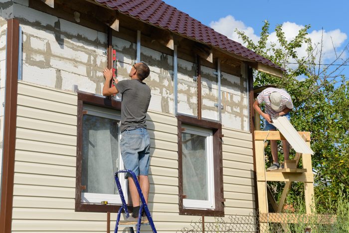 two men work on replacing siding on a residential house