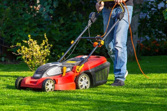a man in jeans mows the grass in the garden with a lawn mower, summer day