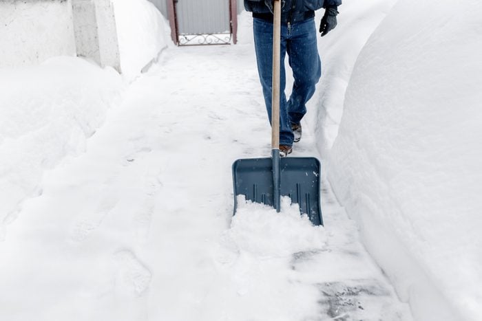 Snow removal, a man cleans the snow with a blue shovel near his house.
