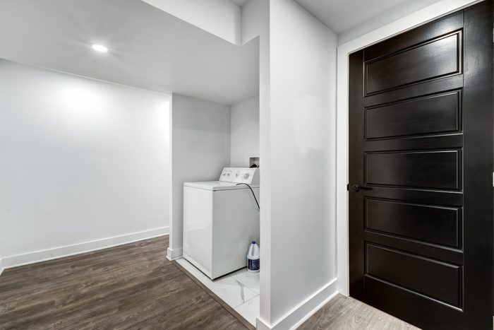 a washing machine in a refinished basement with bright white walls and a wood floor