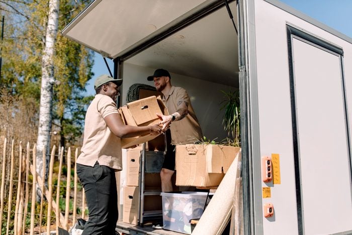 Multiracial movers unloading cardboard boxes from truck during sunny day