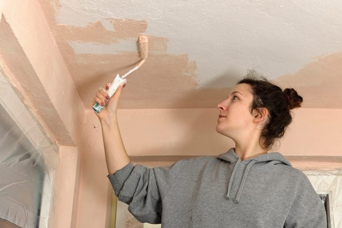 Young woman painting ceiling of an apartment