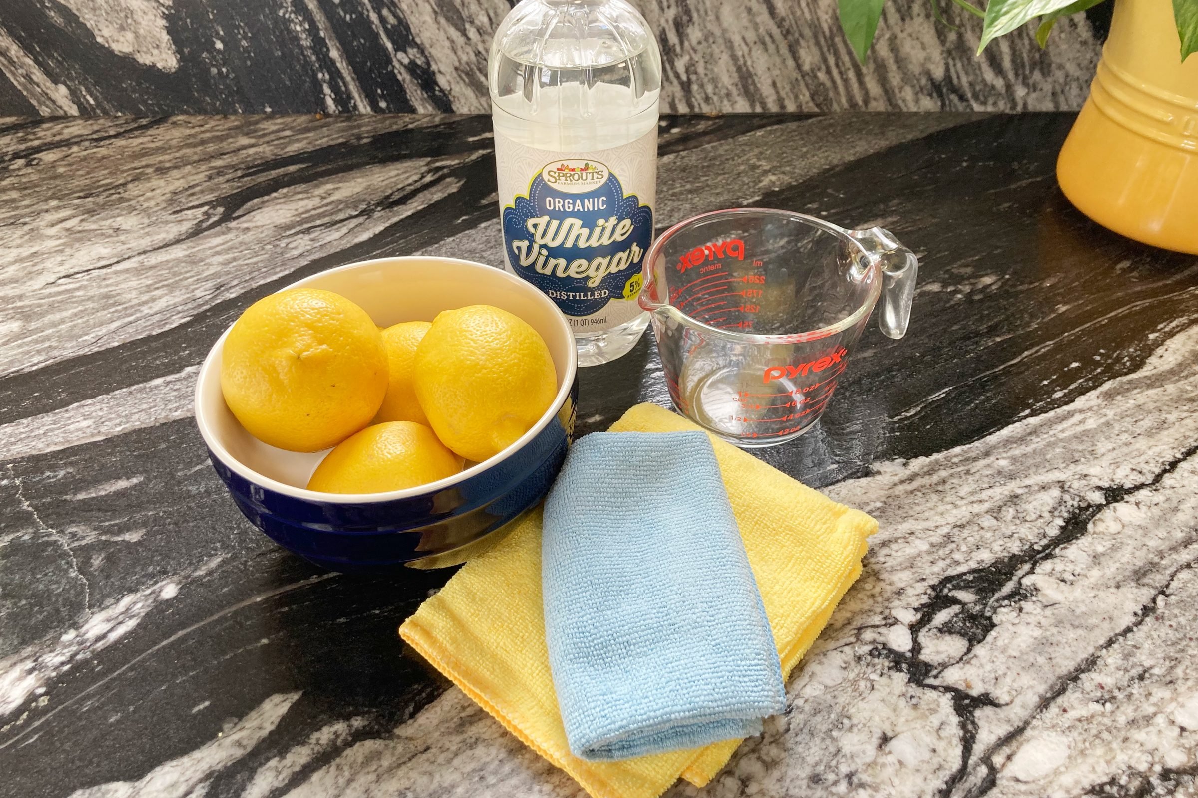 blue bowl of lemons, vinegar, cleaning cloths and measuring cup on a kitchen counter