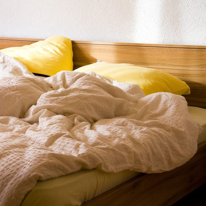 An Unmade Bed With Yellow Pillows In The Morning