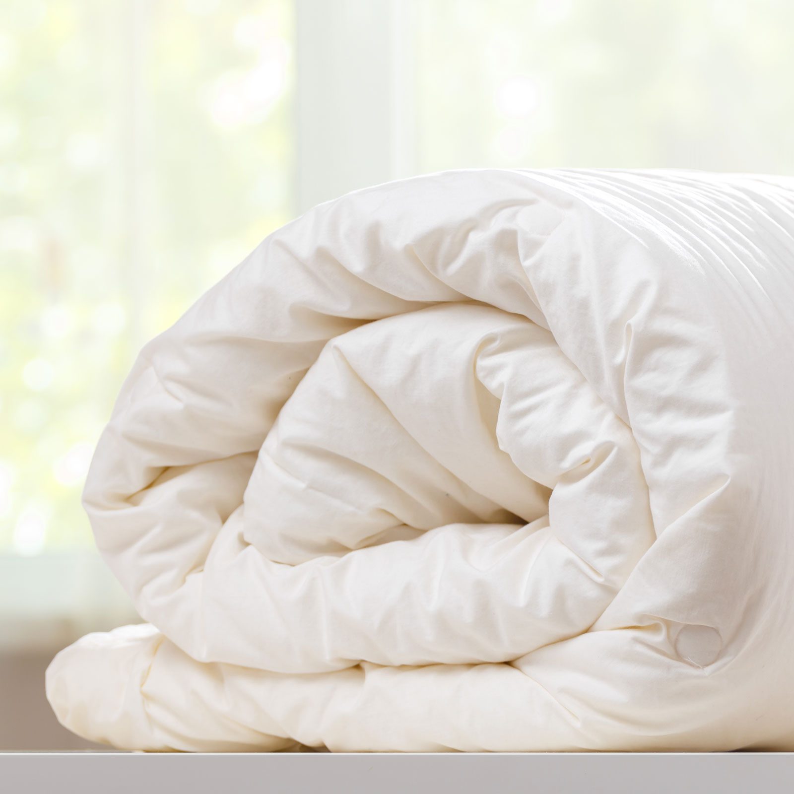 A Folded Rolled Duvet cover Is Lying On The Dresser Against The Background Of A Blurred Window