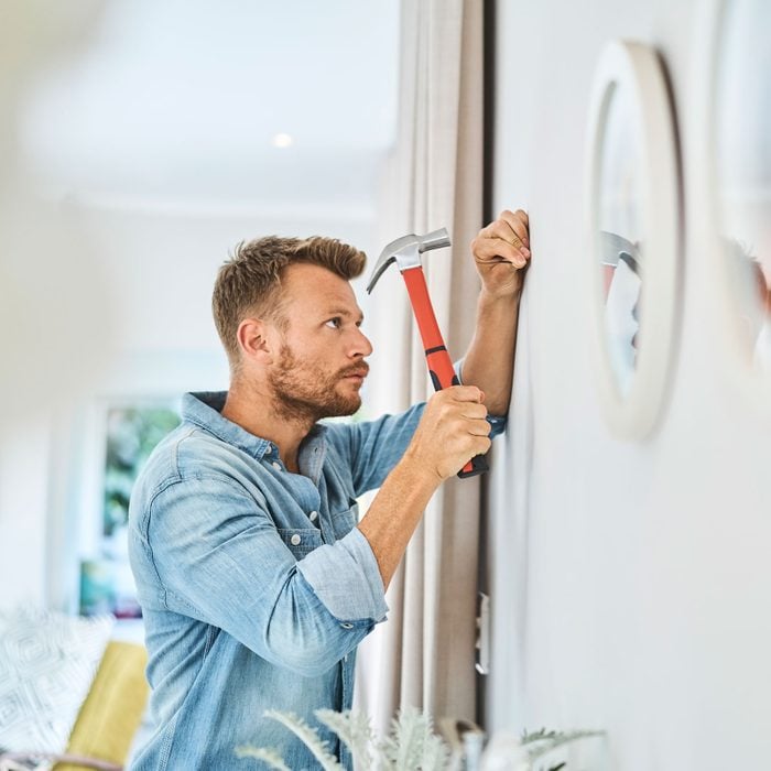 Handsome Young Man Hammering Nail On White Wall