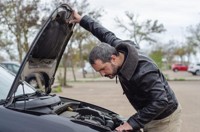 worried mature man looking under the hood of breakdown car